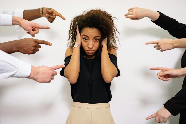A woman experiencing stress from work as several hands point at her from all directions.