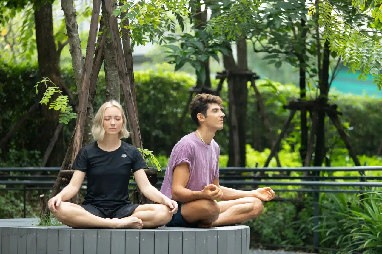 A man and a woman meditating setting in outdoor area at Horizon Rehab Center surrounded by green trees